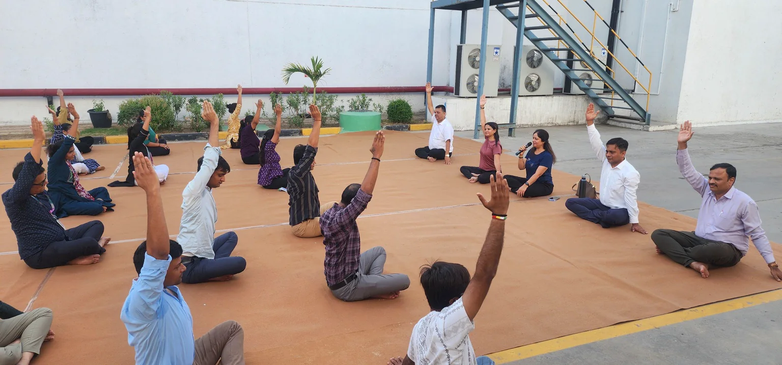 A workplace group practising seated yoga outdoors with an instructor guiding the session