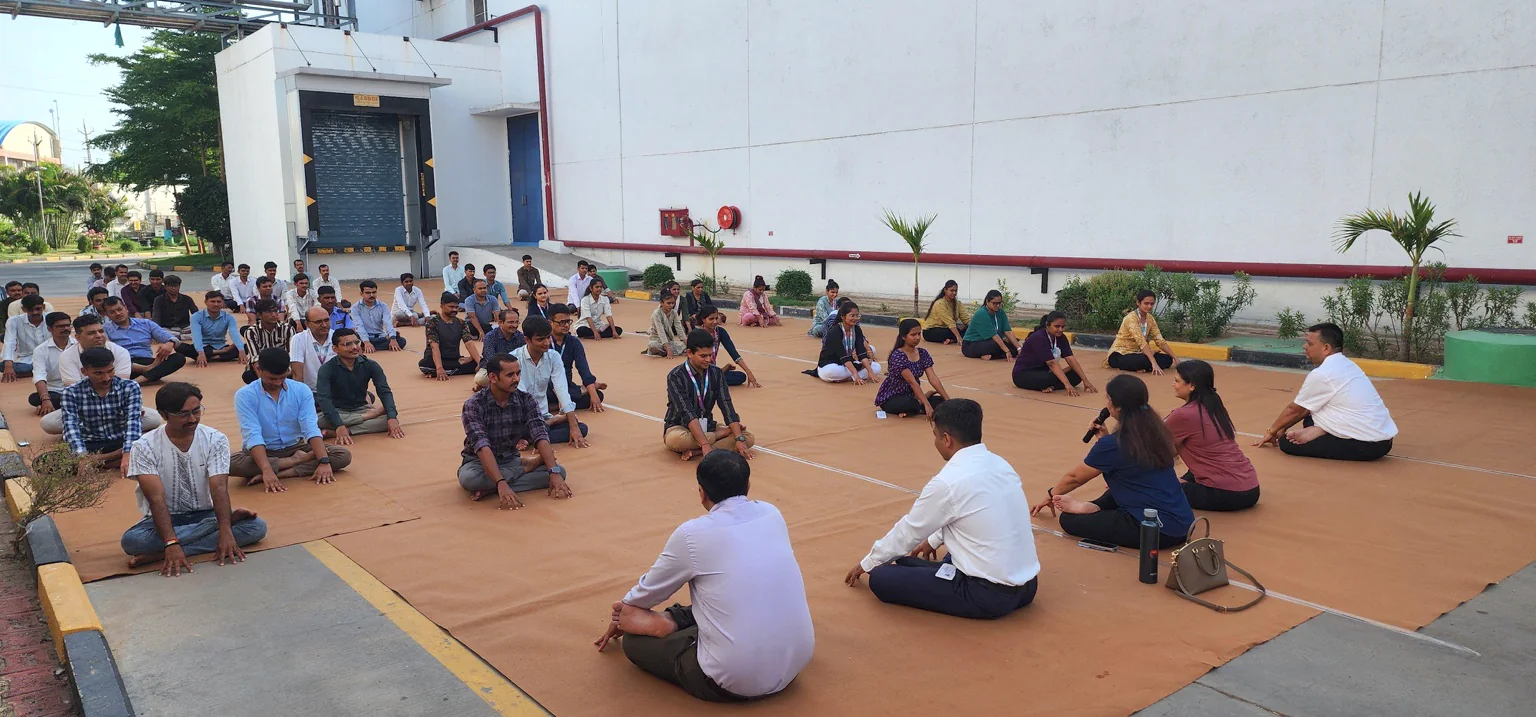 A large workplace group seated outdoors during a guided yoga session